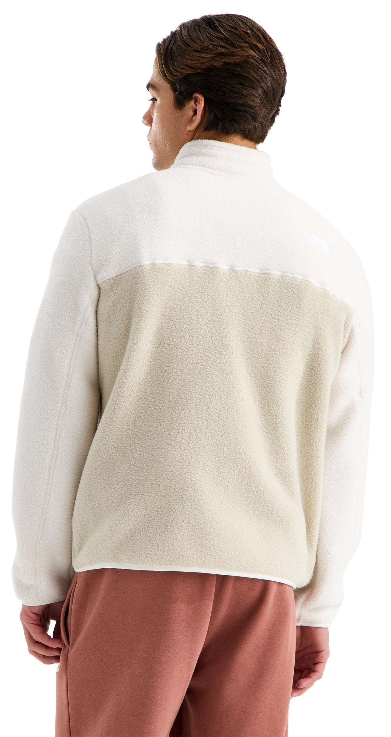 Rear view of a person wearing a two-toned, long-sleeved, collared fleece jacket with a white upper section and a light beige lower section, paired with rust-colored trousers.