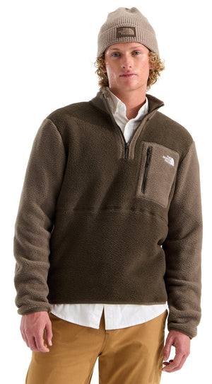 A man wearing a tan beanie, a white collared shirt under a dark olive green quarter-zip fleece pullover with a chest pocket, and khaki pants.