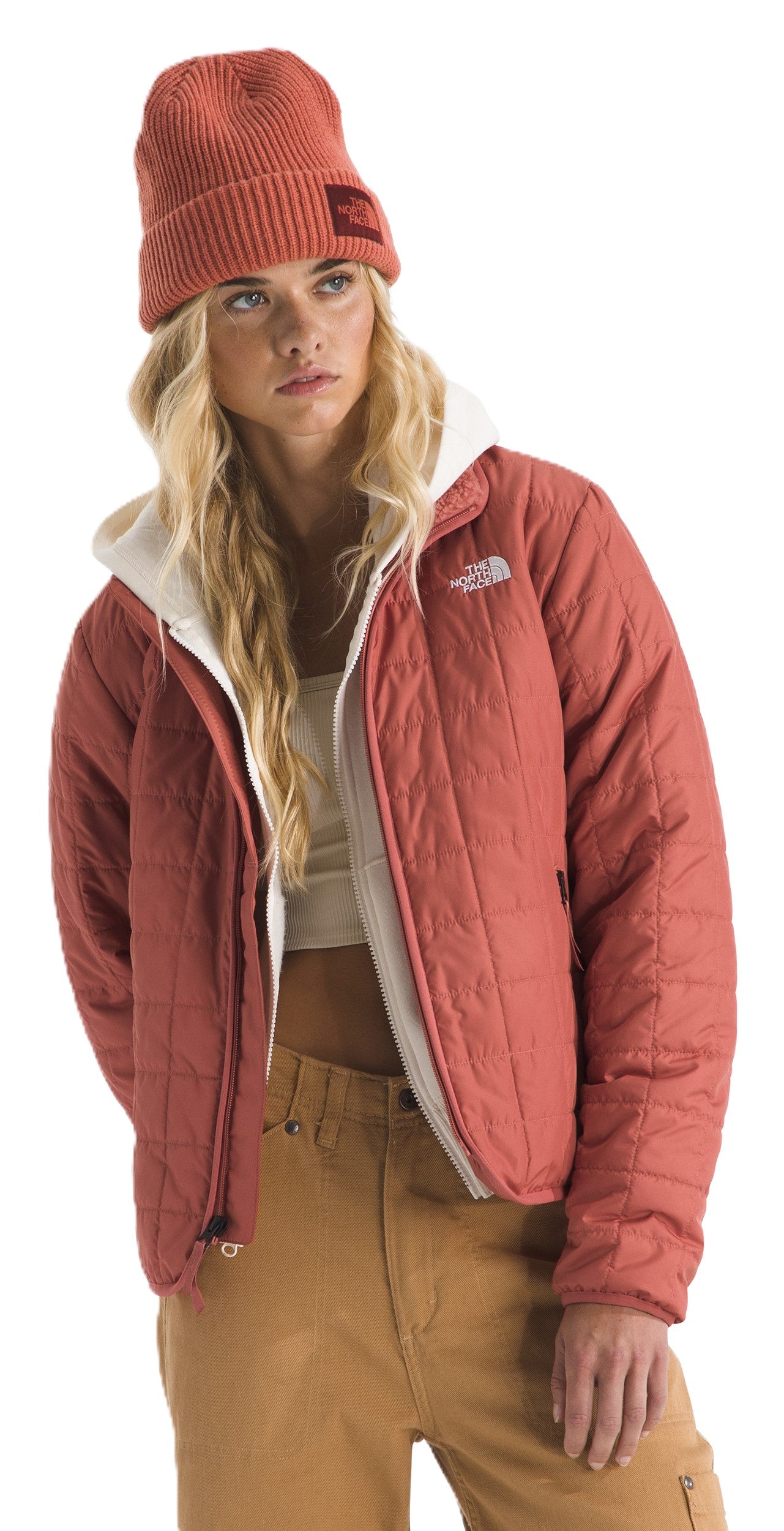 Woman in a red quilted jacket, a cream-colored hoodie, tan pants, and a matching red beanie.