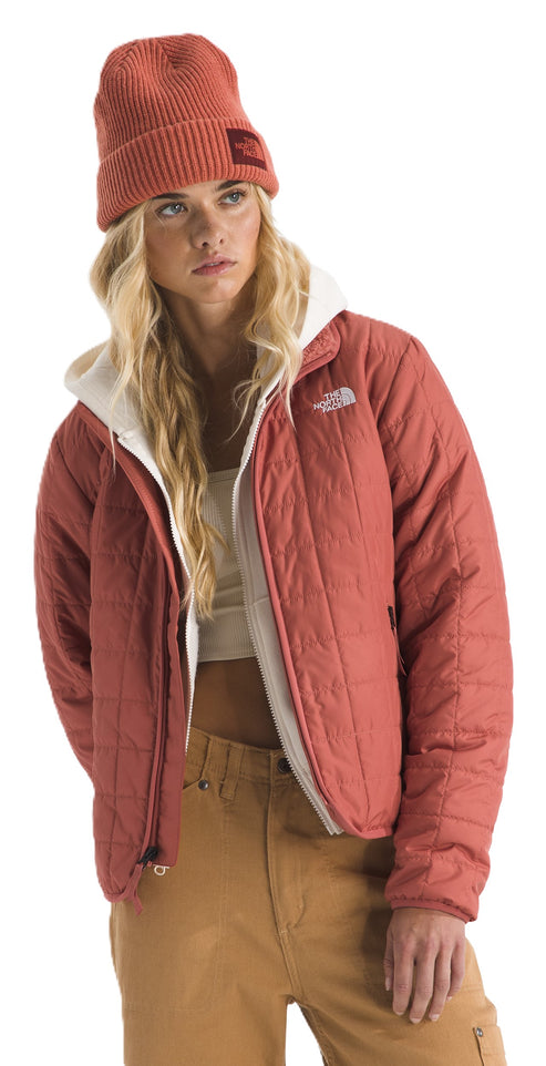 Woman in a red quilted jacket, a cream-colored hoodie, tan pants, and a matching red beanie.