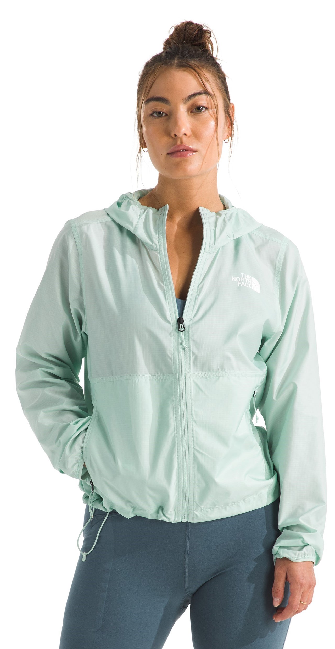 A woman in a light green hooded windbreaker with a full zipper and a cinchable hem and gray leggings.