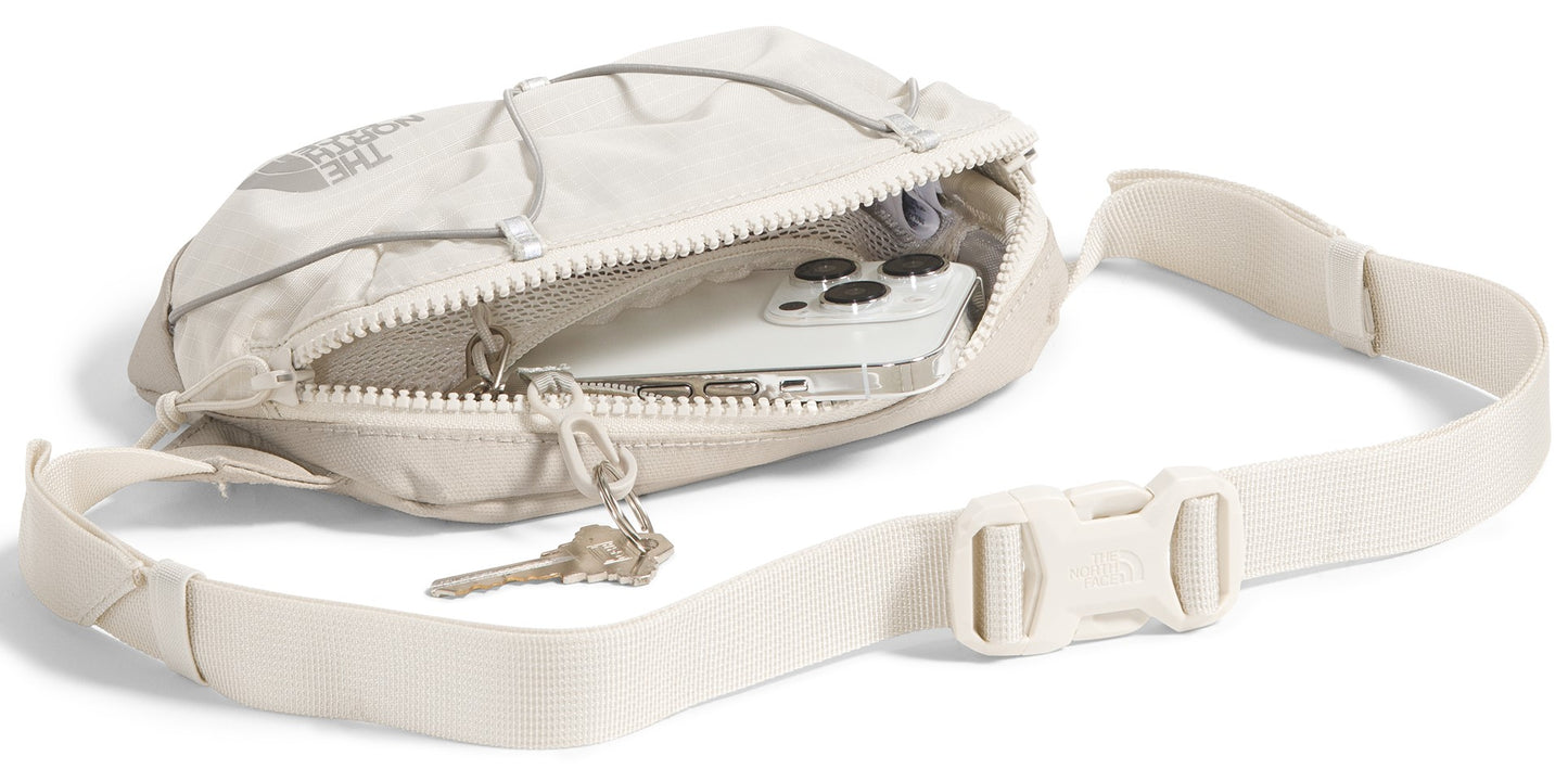 A beige fanny pack with a white strap, white buckle, keys and a phone inside of it.