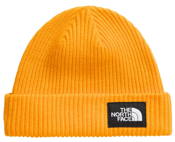 Close-up of a ribbed, yellow knit beanie with a black square tag showing white text 'The North Face'.