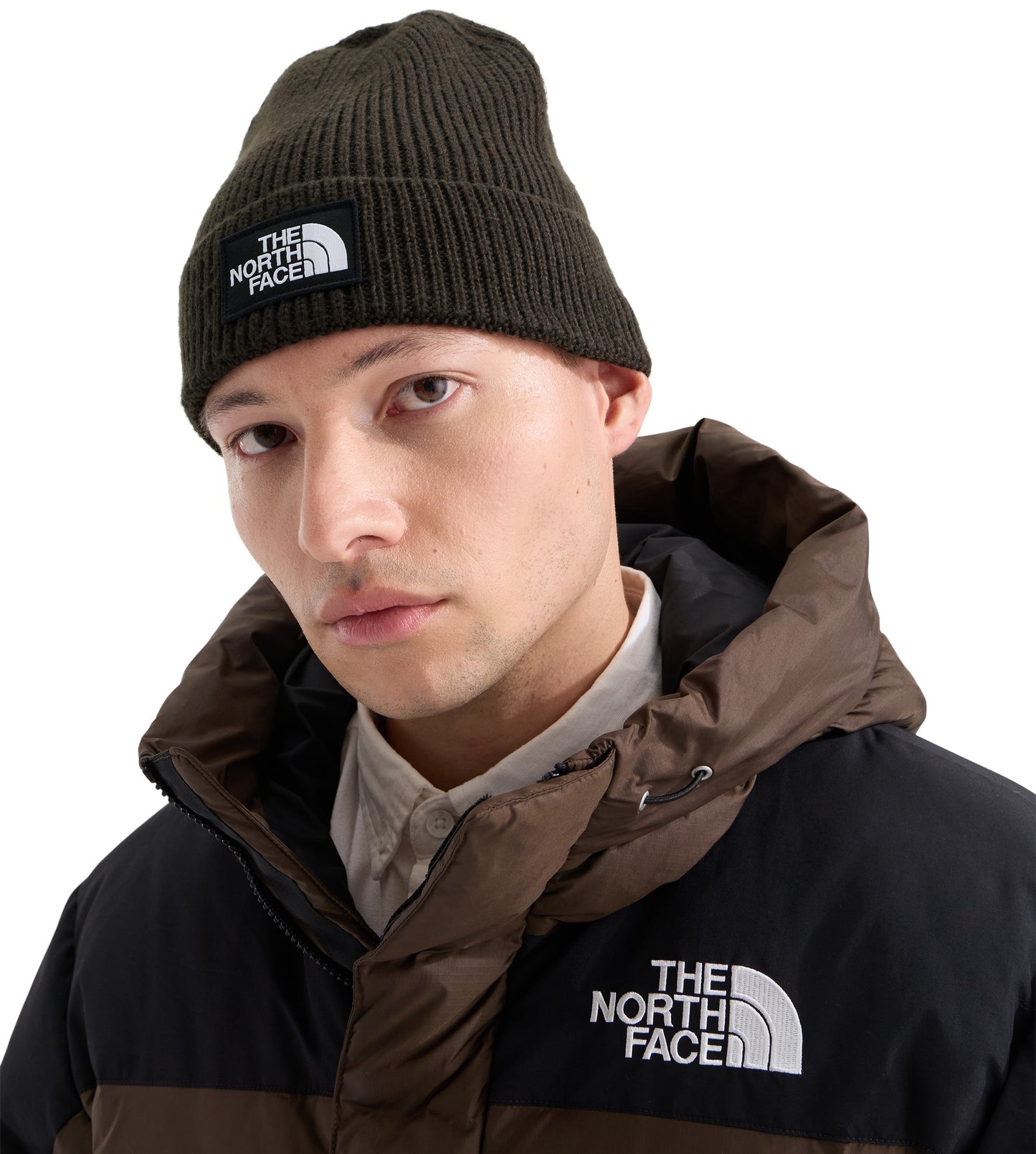 A man wearing an olive-green ribbed beanie with a square patch reading THE NORTH FACE on the front, and a dark brown and black hooded winter jacket with the brand logo on the chest.