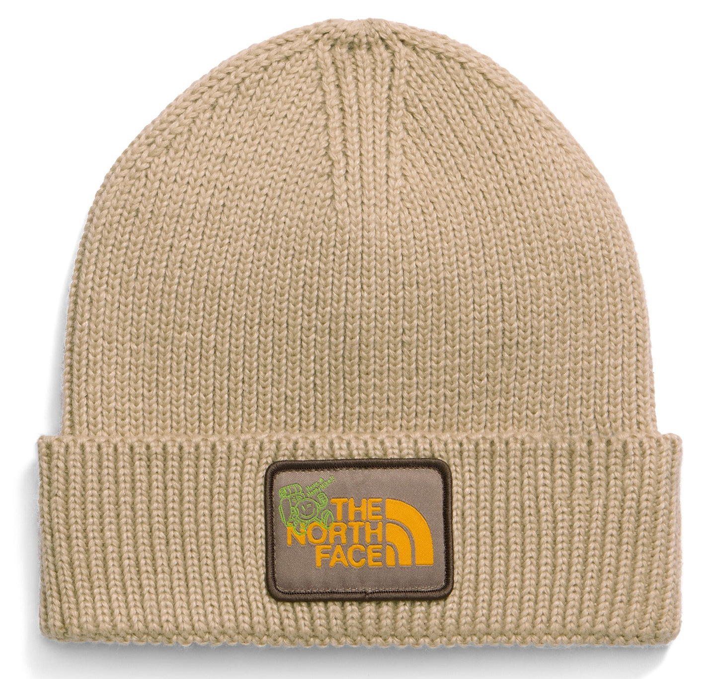 A tan knit beanie with a folded cuff featuring a brown rectangular patch with yellow text reading THE NORTH FACE and a small green graphic icon.