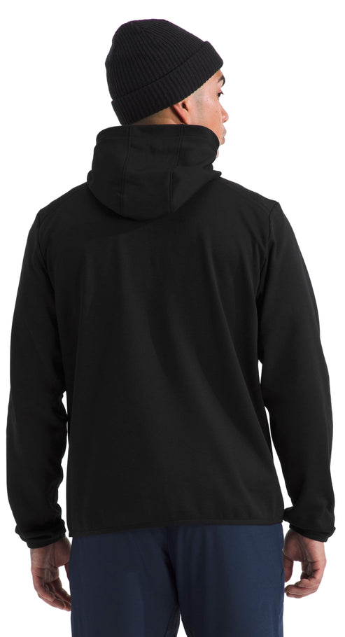A person wearing a black beanie and a black hooded jacket, with dark blue pants. The jacket has long sleeves and the hood is up.