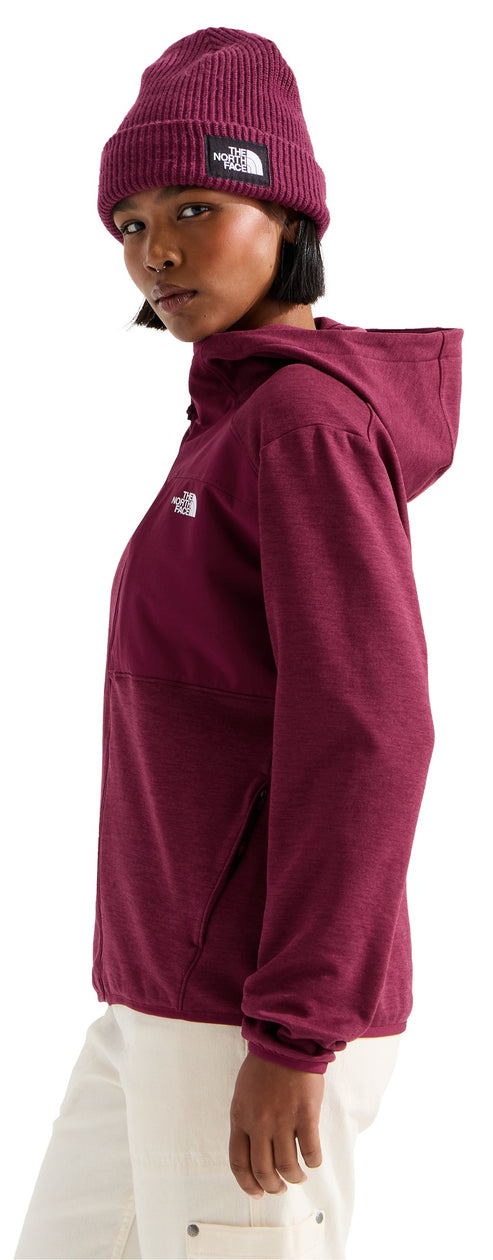 A person viewed from the side wearing a dark berry colored knit beanie with a rectangular patch and a matching hooded jacket over white pants.