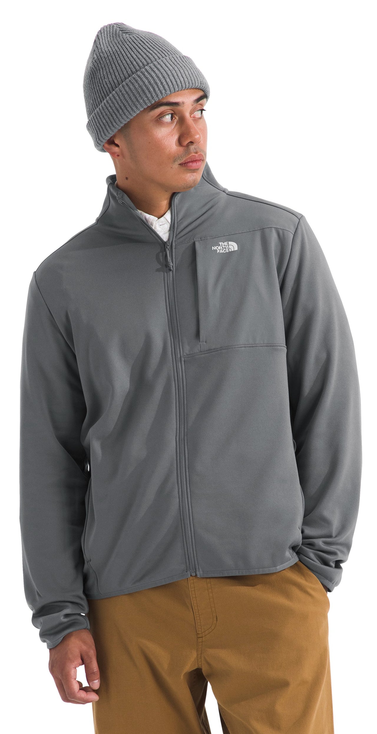 Man wearing a grey jacket and beanie, with tan pants. The jacket has a chest pocket with a small logo near it.