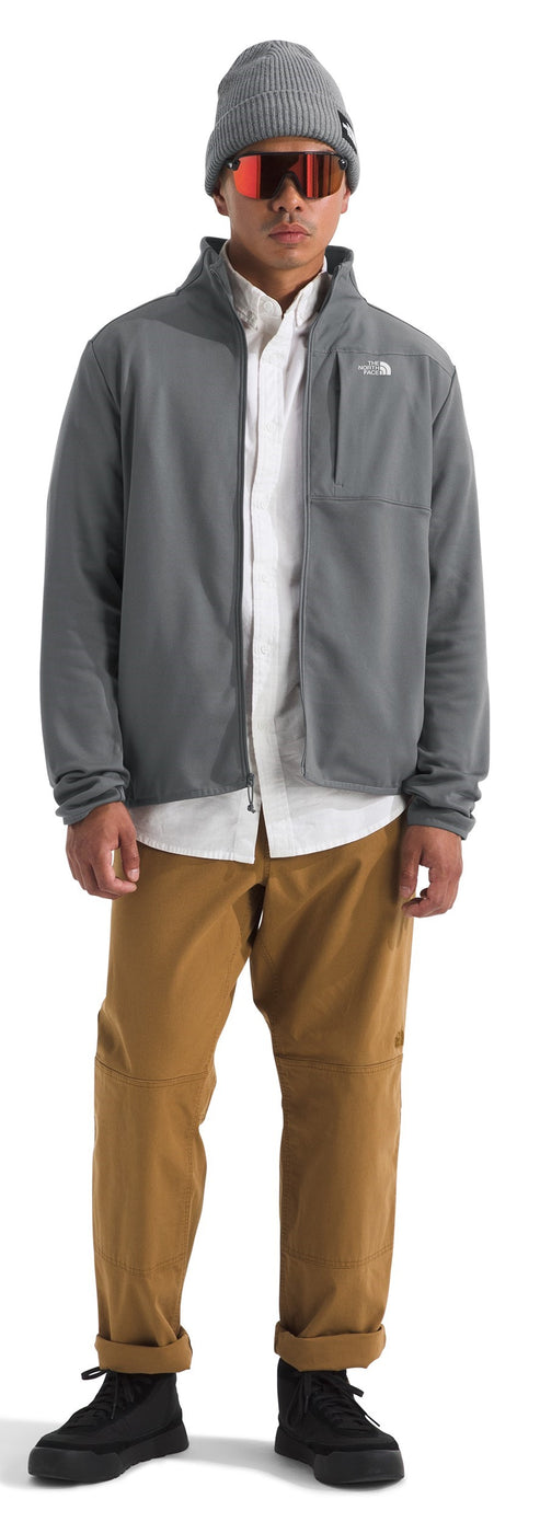 A person in a grey jacket, white shirt, and brown pants wearing a grey beanie and orange goggles.