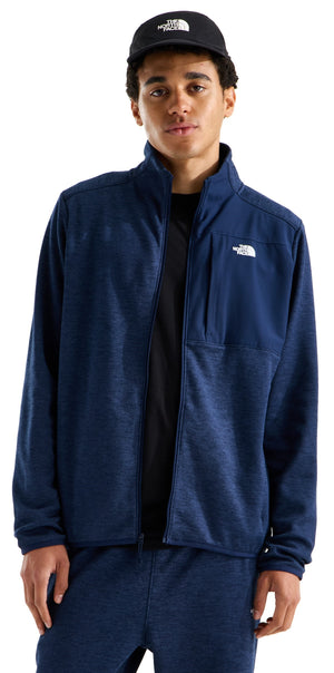 A man wearing a blue heathered zip-up track jacket and a black baseball cap with white text on the front.