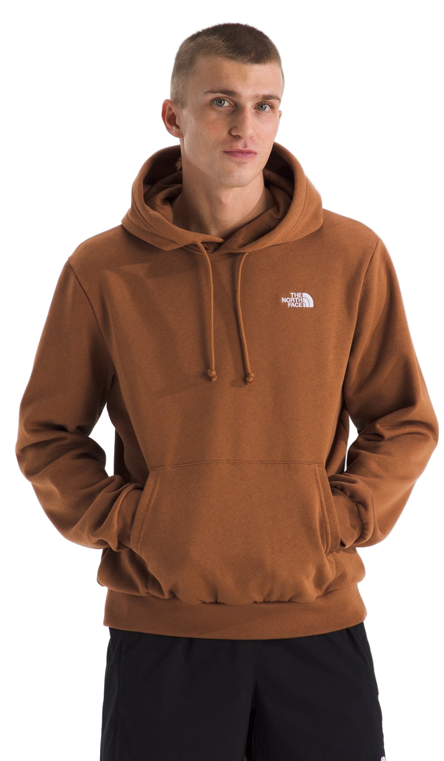A man wearing a brown hoodie with a hood up and a kangaroo pocket, and the logo in white on the upper left chest.