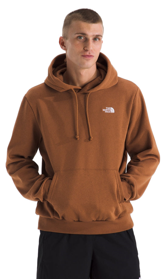 A man wearing a brown hoodie with a hood up and a kangaroo pocket, and the logo in white on the upper left chest.
