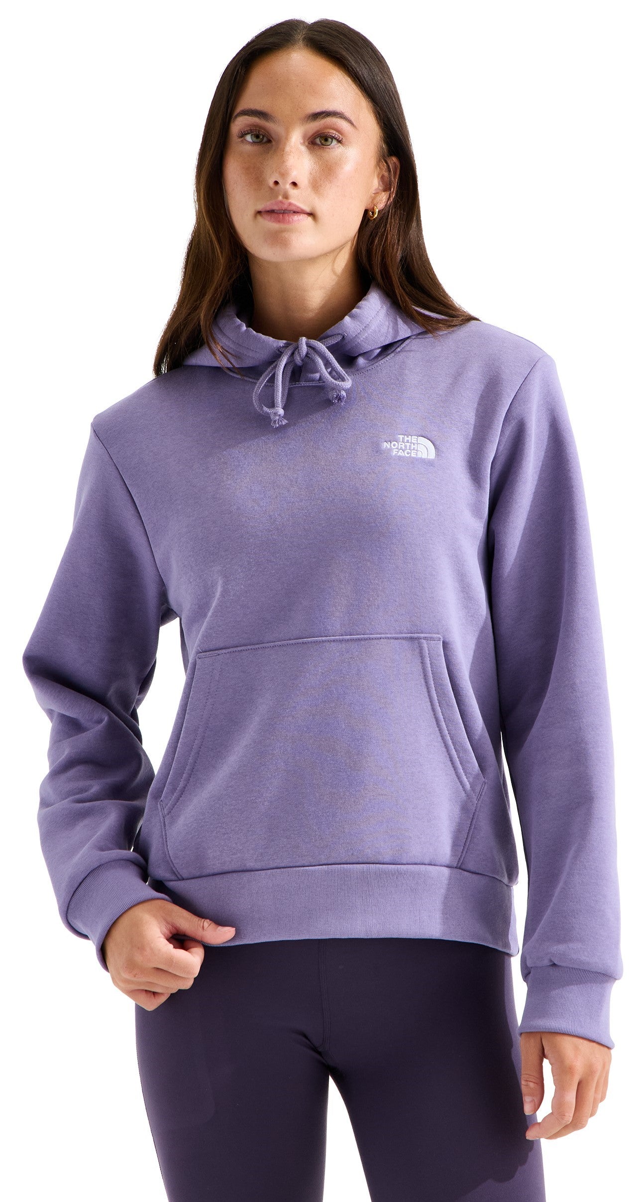 A woman wearing a lavender-colored, long-sleeved hooded sweatshirt with a kangaroo front pocket and a small white logo on the upper left chest, paired with dark purple leggings.