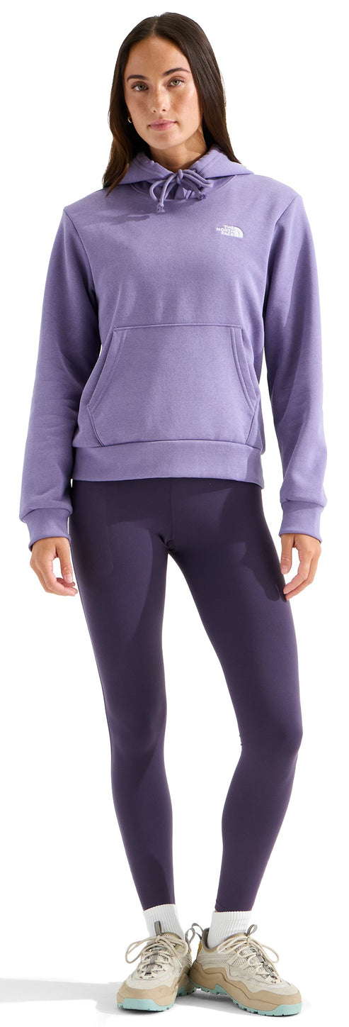 A woman wearing a lavender pullover hoodie with a white logo on the chest, dark purple leggings, and beige athletic shoes.