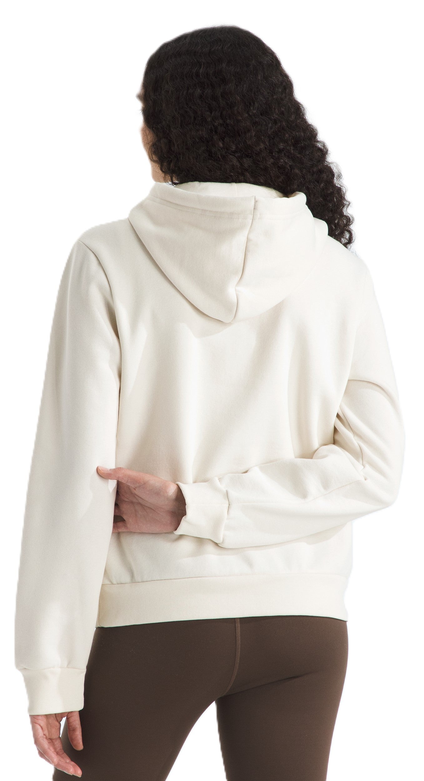 A person faces away from the viewer and has their hands crossed behind their lower back. They are wearing a light-colored hooded sweatshirt and brown pants.