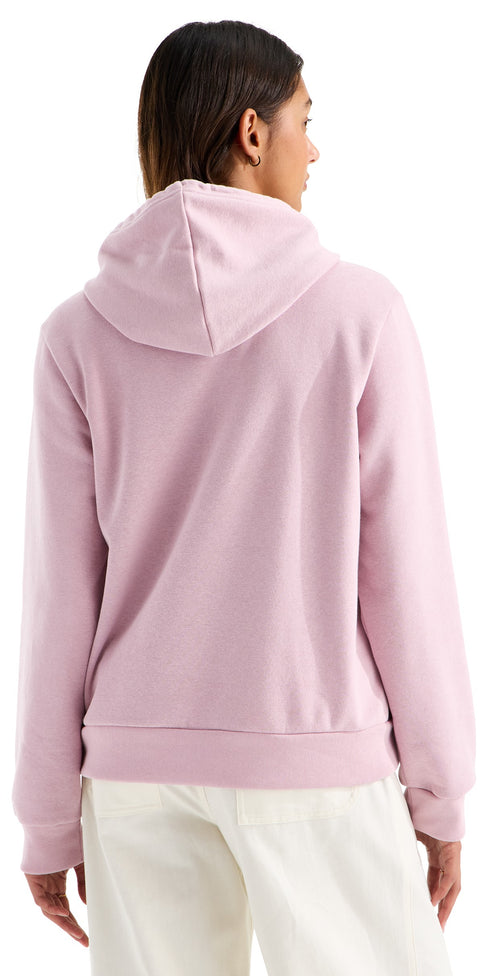 A back view of a woman wearing a light pink, long-sleeved hooded sweatshirt with a hood up, paired with white pants.