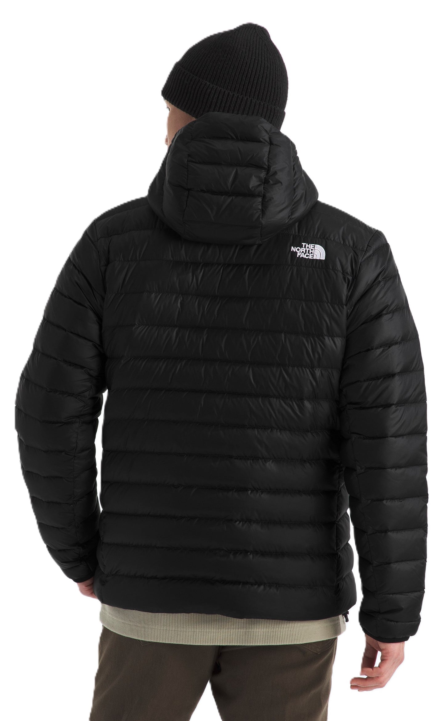 A person wearing a black hooded puffer jacket with a logo on the upper back and a black beanie.