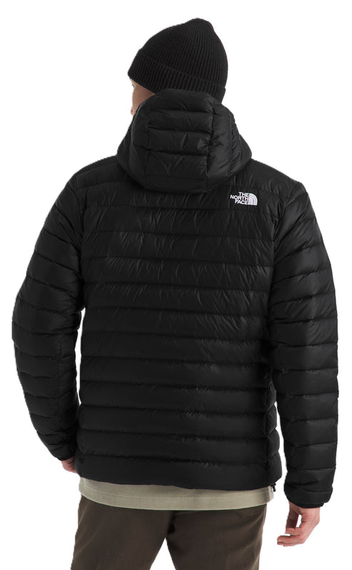 A person wearing a black hooded puffer jacket with a logo on the upper back and a black beanie.