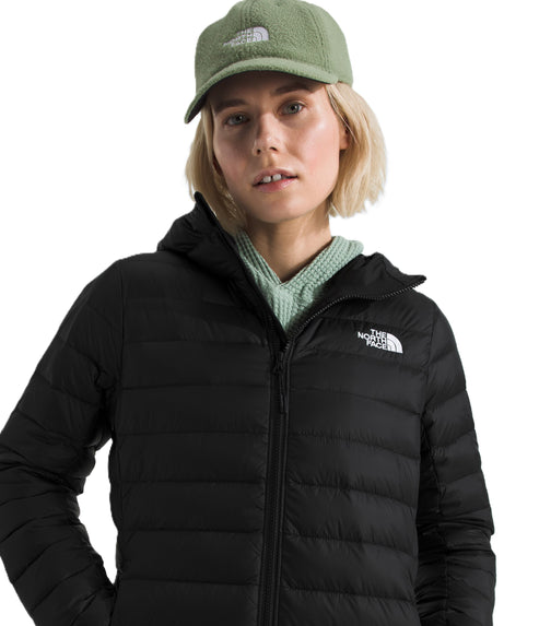 A person wearing a black zip up hooded puffer jacket and a green cap.