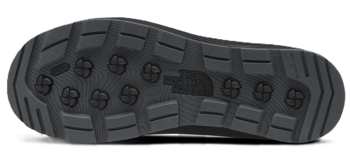 A view of the black rubber outsole of a shoe, featuring a rugged tread pattern with rectangular lugs and a series of circular, cross-shaped traction elements in the center. The North Face logo is molded into the middle of the sole.
