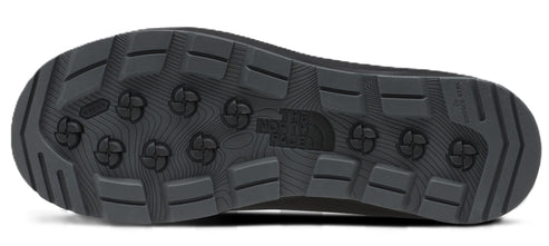 A view of the black rubber outsole of a shoe, featuring a rugged tread pattern with rectangular lugs and a series of circular, cross-shaped traction elements in the center. The North Face logo is molded into the middle of the sole.