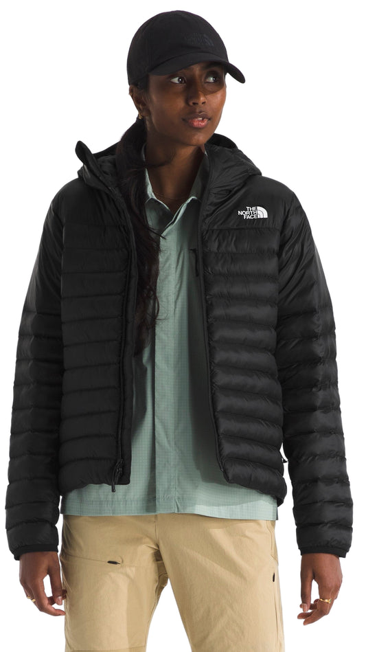 A person wearing a black puffer jacket with a hood, light green shirt, khaki pants, and a black cap.