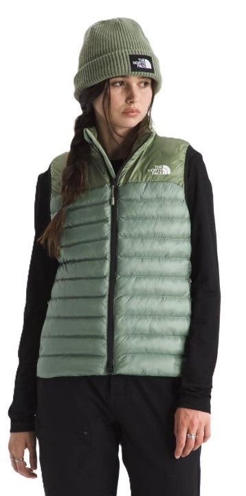 A person wearing a sage green puffer vest and a matching beanie.