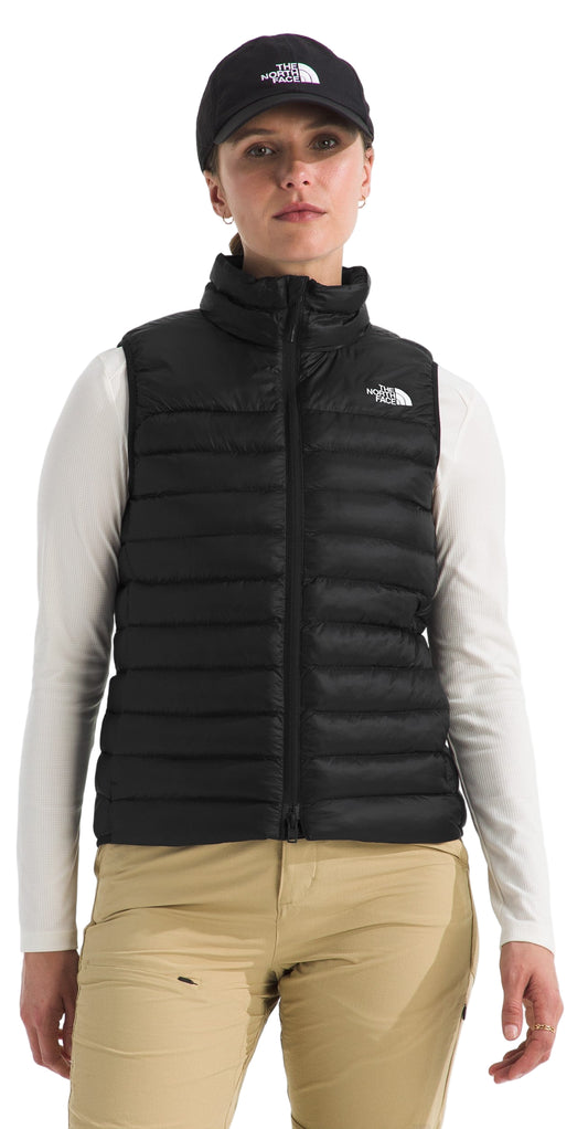 A woman wearing a black vest, a black cap, a white long-sleeve shirt, and khaki pants.