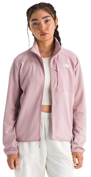 A woman wearing a zippered, light purple jacket with a white logo on the upper right side, zipped up over a white crop top, and white pants.