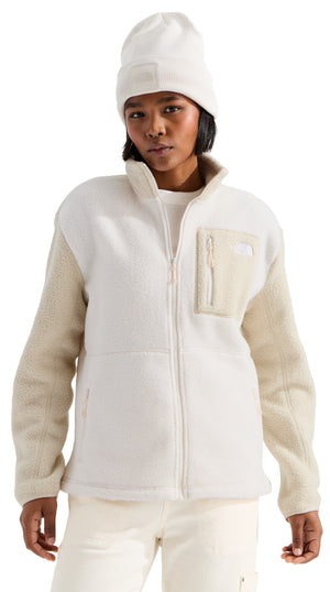 A person wearing a cream-colored knit beanie and a full-zip fleece jacket featuring a mix of smooth and textured fabric panels, a chest pocket, and a mock neckline.
