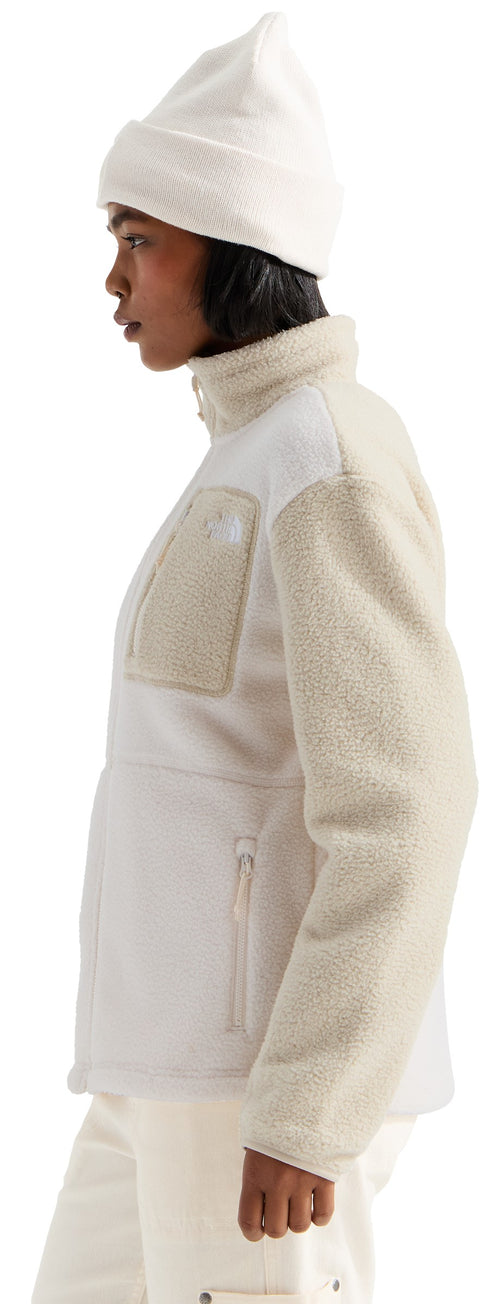 A profile view of a person wearing a cream-colored knit beanie, a high-neck fleece jacket with textured, light beige sleeves and a matching patch pocket on the chest, paired with cream trousers.