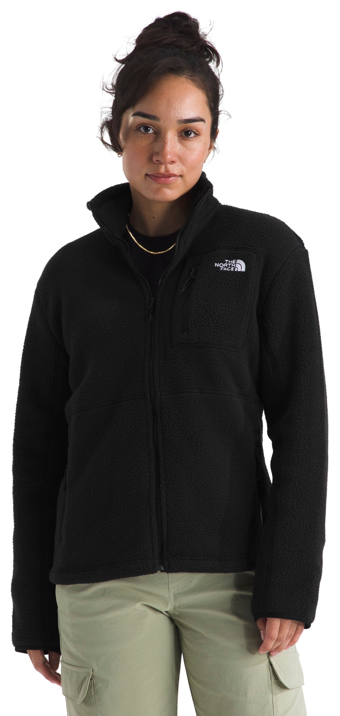 A woman wearing a black zip-up fleece jacket with a high collar and The North Face logo on the left chest, paired with light olive green cargo pants.