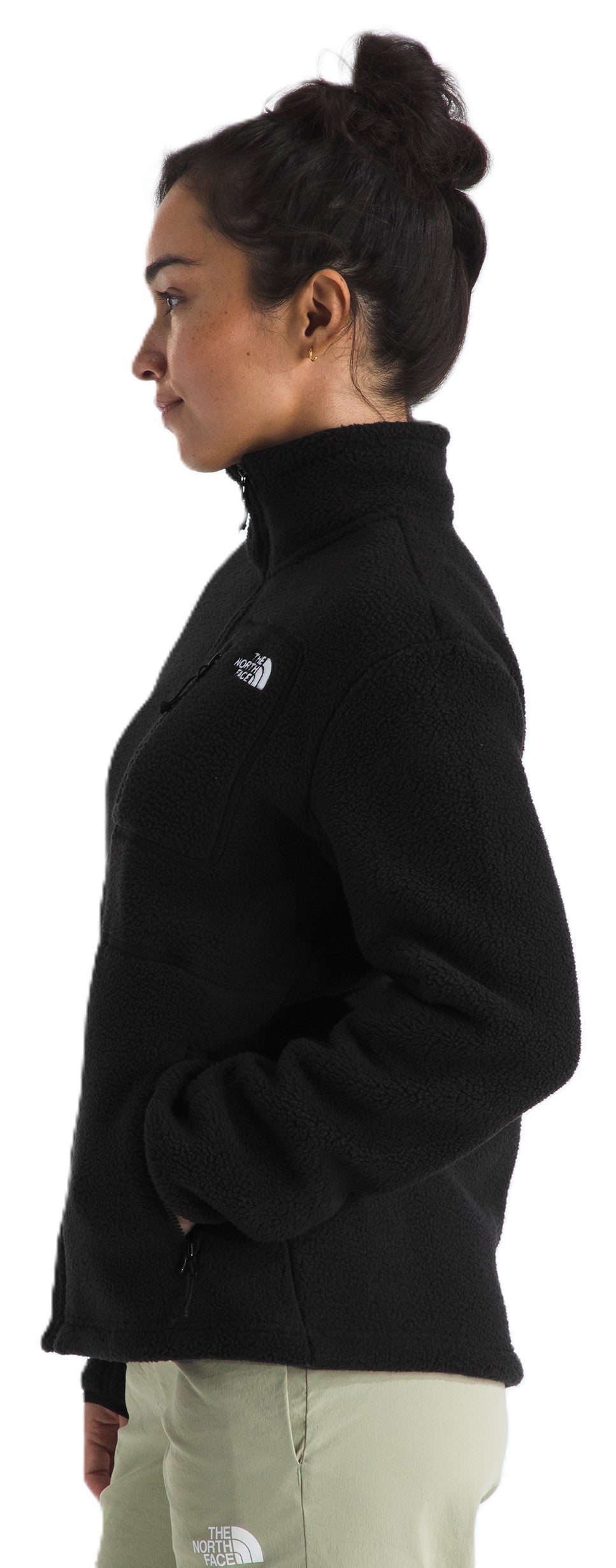 A side view of a person wearing a black fleece zip-up jacket with a white logo on the chest and light-colored pants.