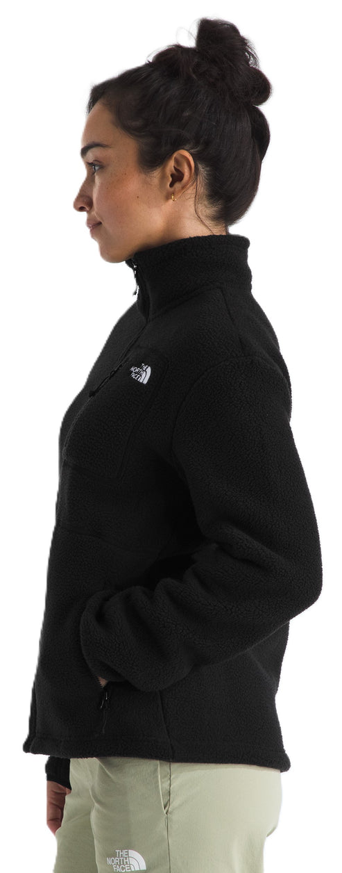 A side view of a person wearing a black fleece zip-up jacket with a white logo on the chest and light-colored pants.