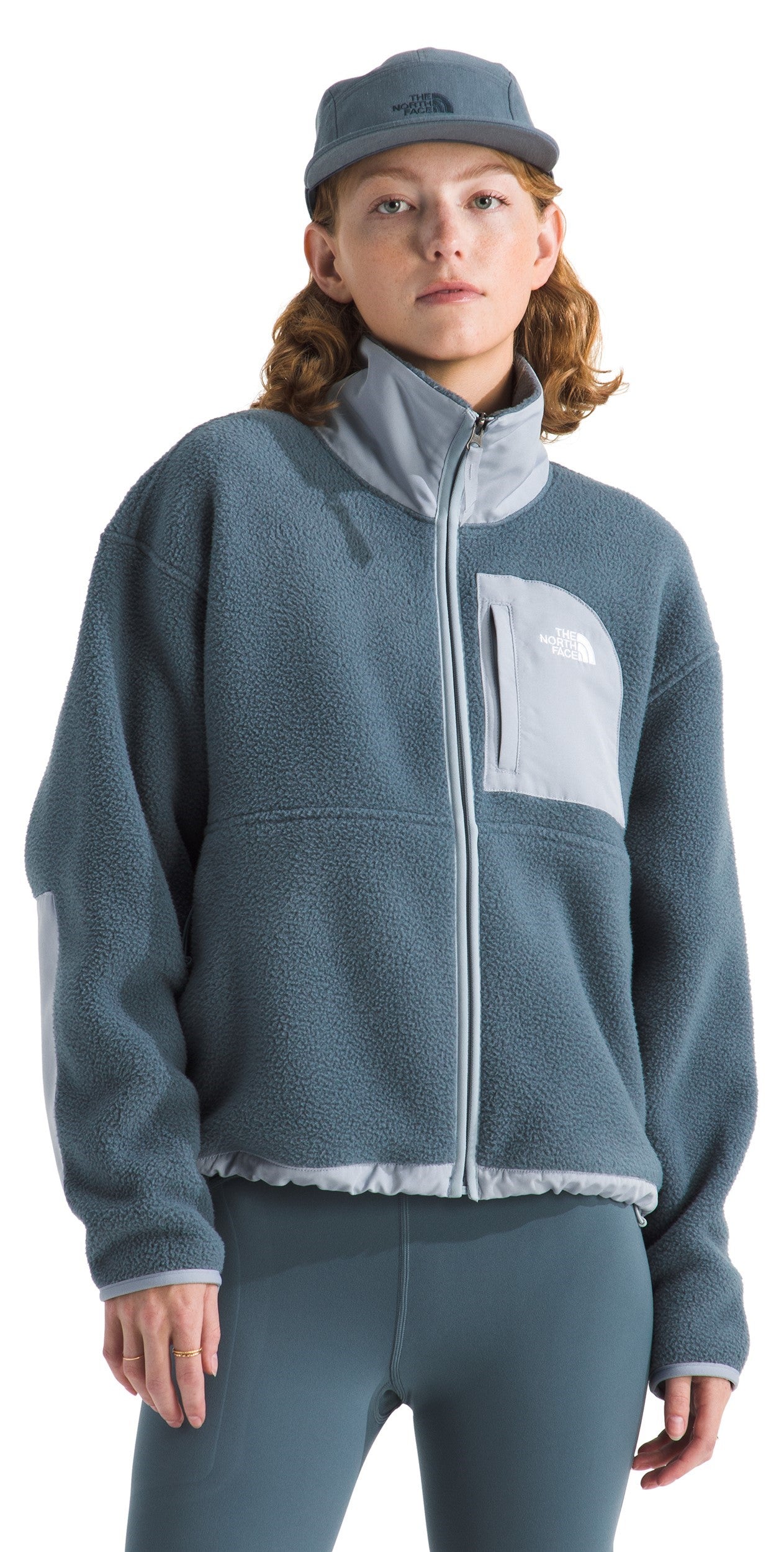 A woman wearing a blue fleece jacket, matching hat, and leggings, the jacket has a gray panel on the chest.