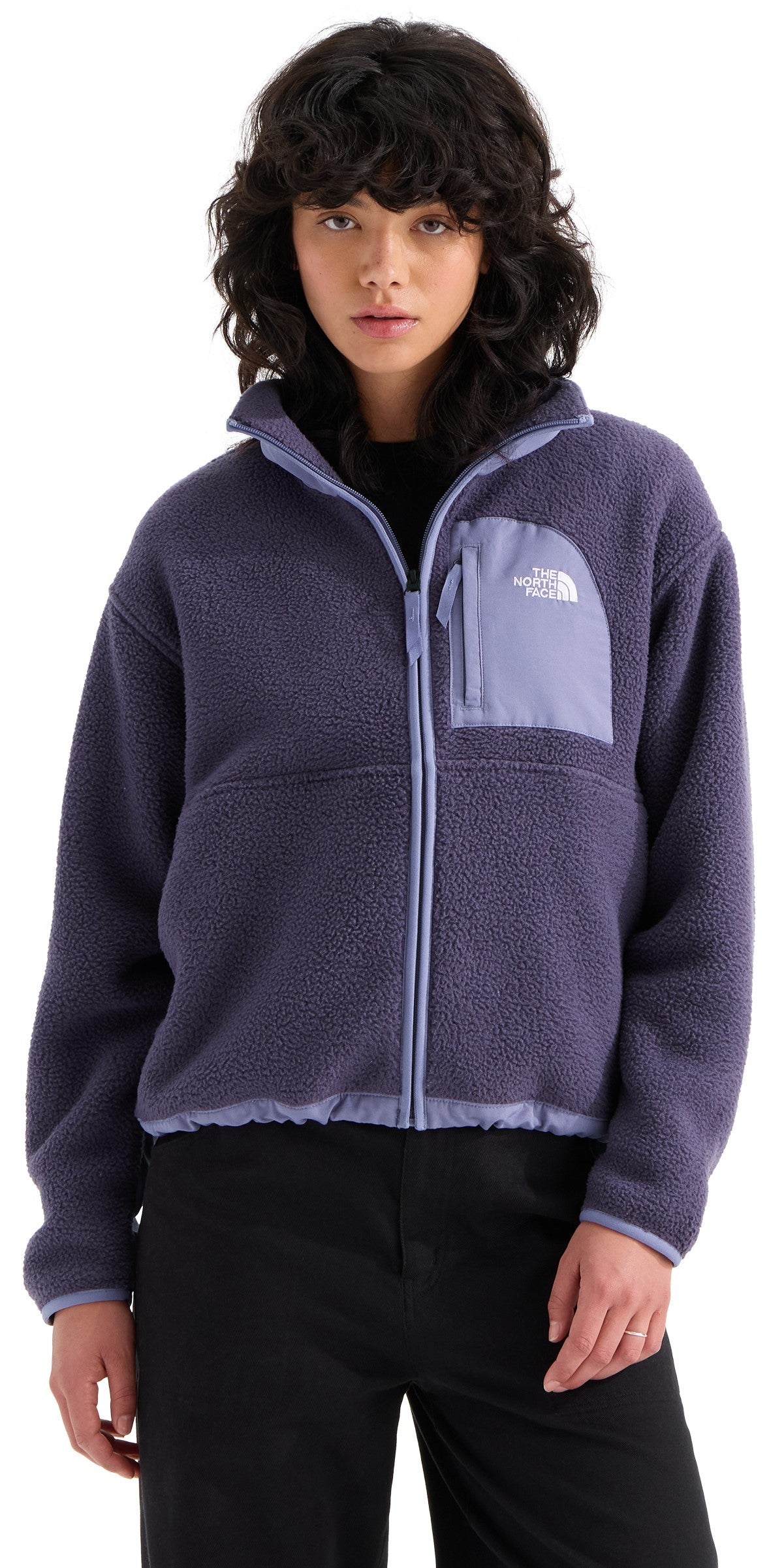 A person wearing a dark blue, textured fleece jacket with a high collar, a light purple zippered chest pocket with a white logo, and light purple trim along the zipper and hem.