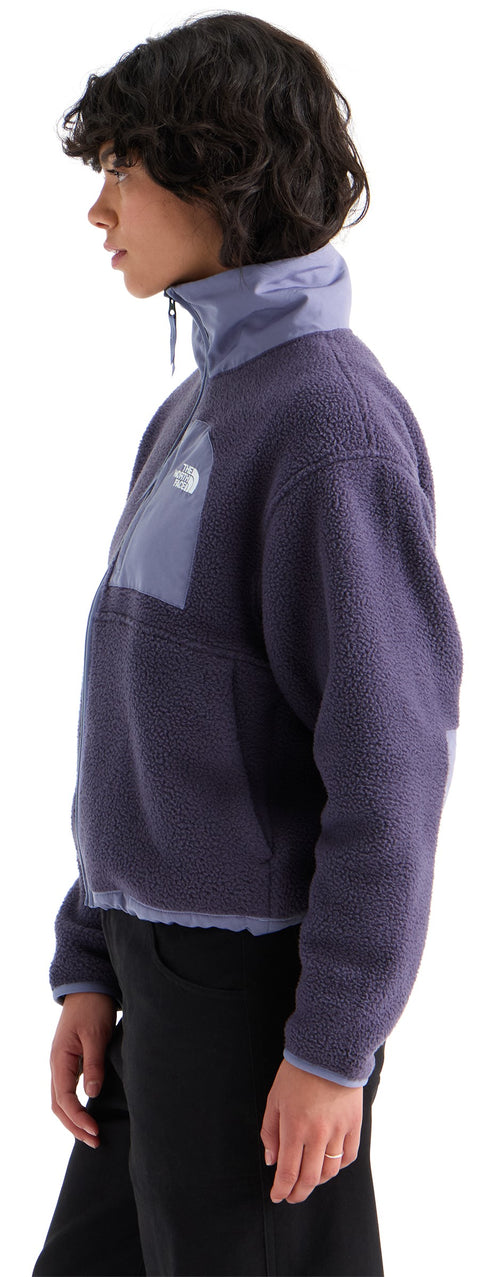 A profile view of a woman wearing a dark purple fleece half-zip jacket with a high collar, featuring a smooth textured panel on the chest and black pants.