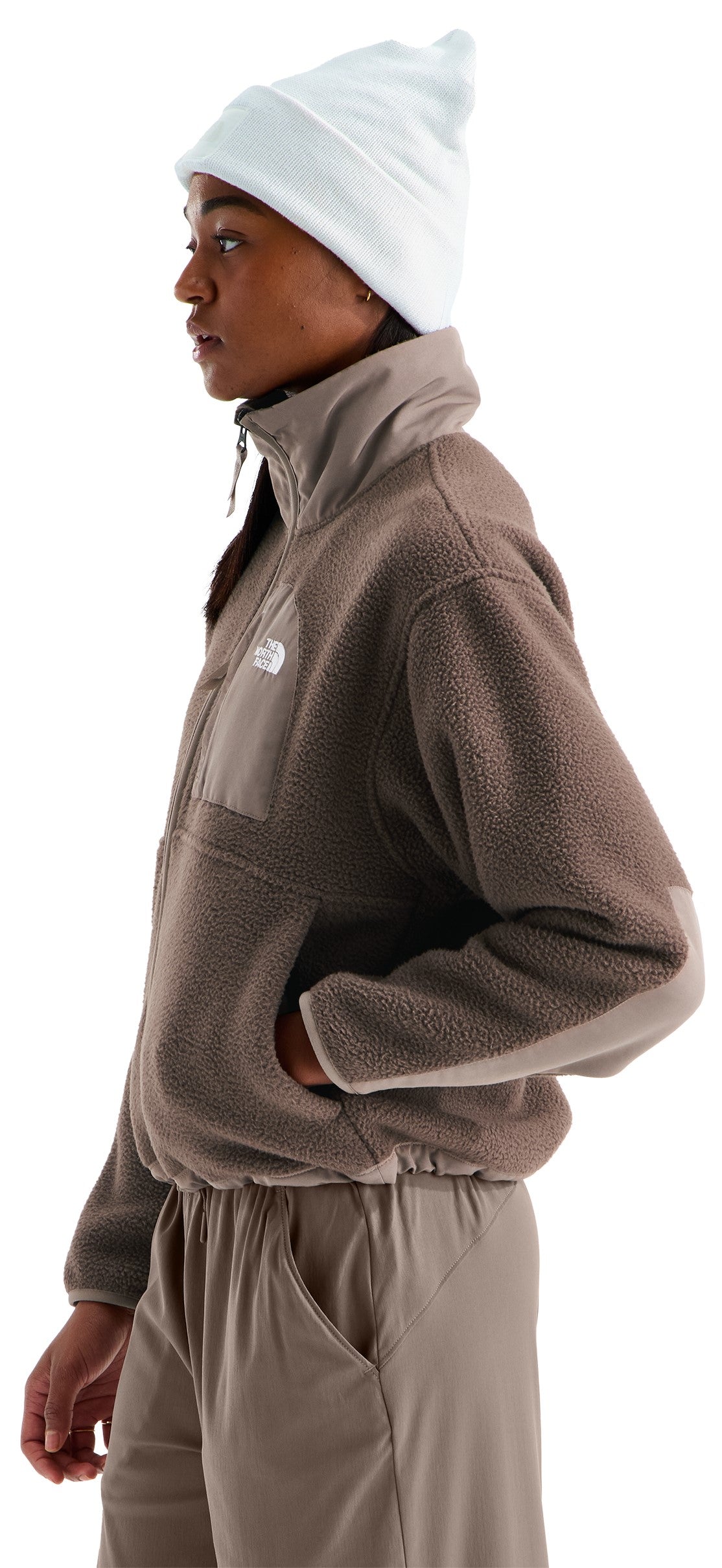 A profile view of a person wearing a beige, textured fleece quarter-zip jacket with a stand-up collar and matching beige pants, paired with a plain light-colored beanie.