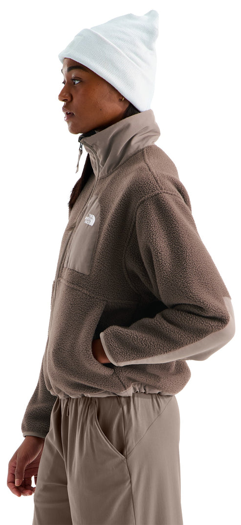 A profile view of a person wearing a beige, textured fleece quarter-zip jacket with a stand-up collar and matching beige pants, paired with a plain light-colored beanie.