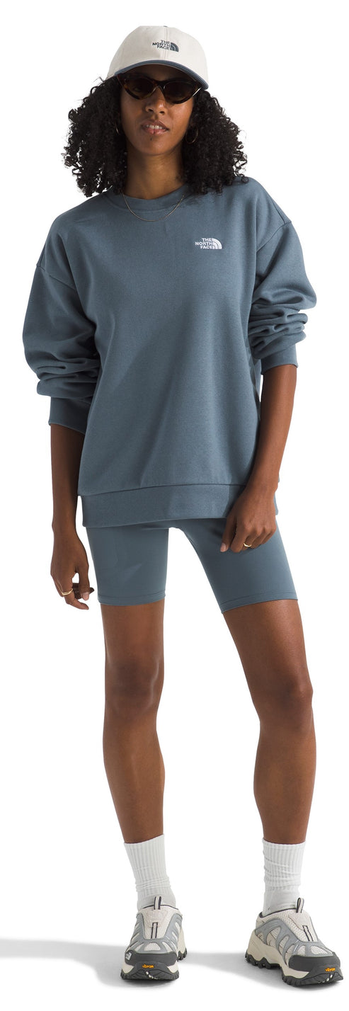 A woman wears a matching set of a sweatshirt and biker shorts, accessorized with a baseball cap, sunglasses, white socks, and sneakers.