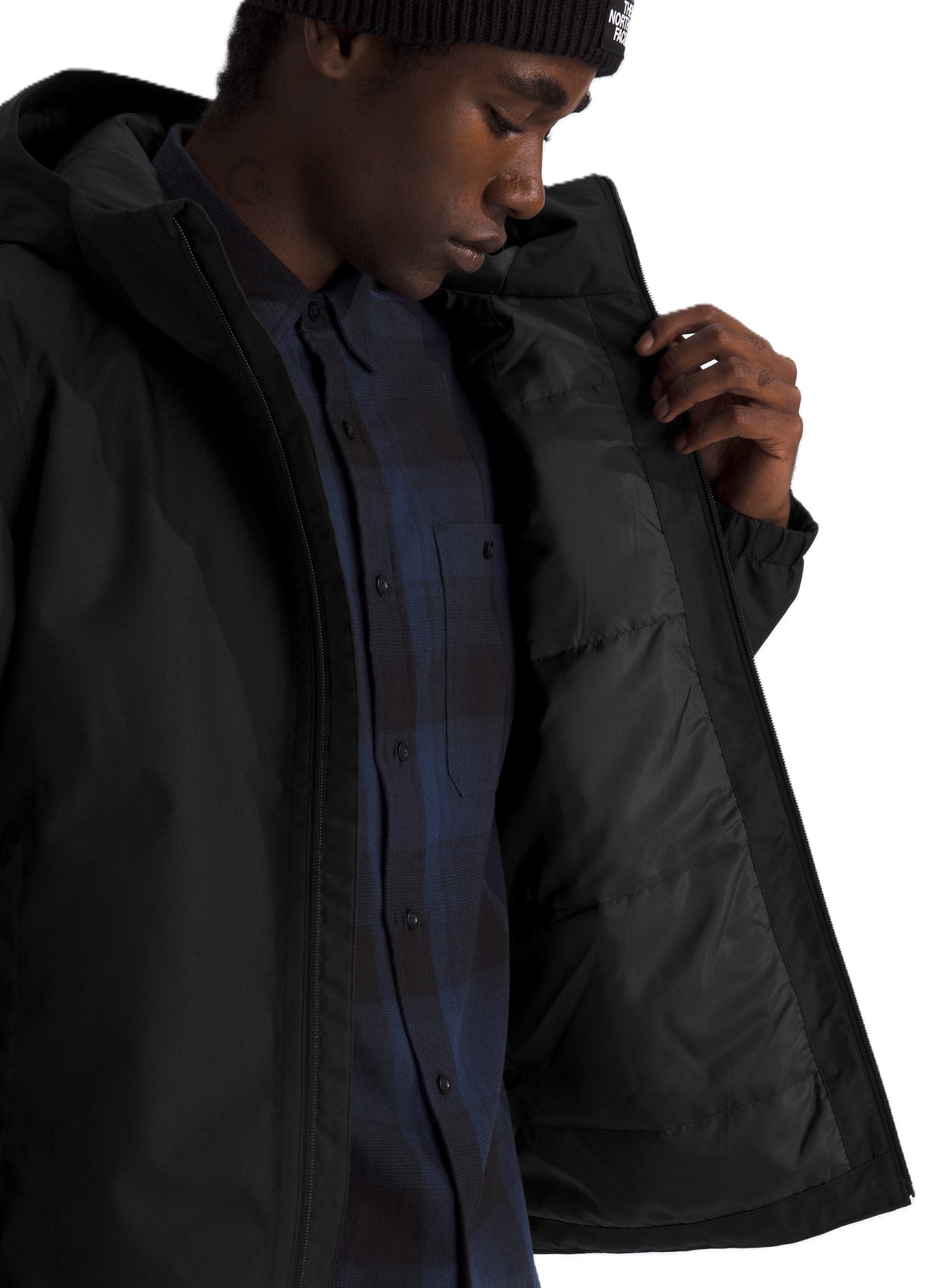 A man wearing a black hooded parka with a quilted inner lining over a dark blue flannel shirt and a black knit beanie.
