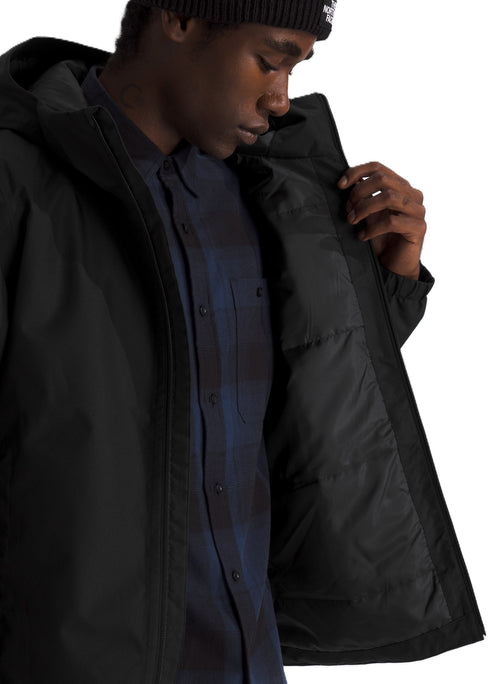 A man wearing a black hooded parka with a quilted inner lining over a dark blue flannel shirt and a black knit beanie.