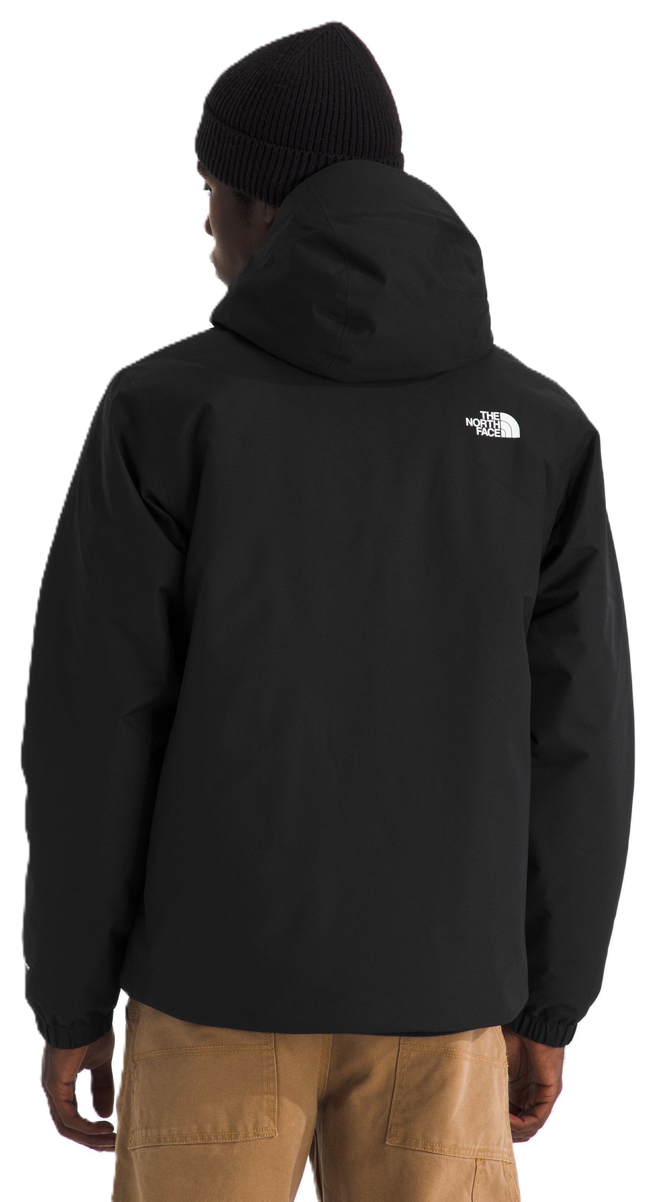 A back view of a person wearing a solid black hooded jacket with a small white logo on the upper right shoulder, a black beanie, and tan trousers.