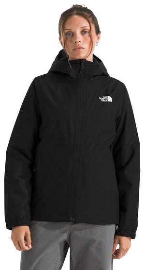 A woman wearing a black hooded, water-resistant outdoor jacket with a white logo on the chest.