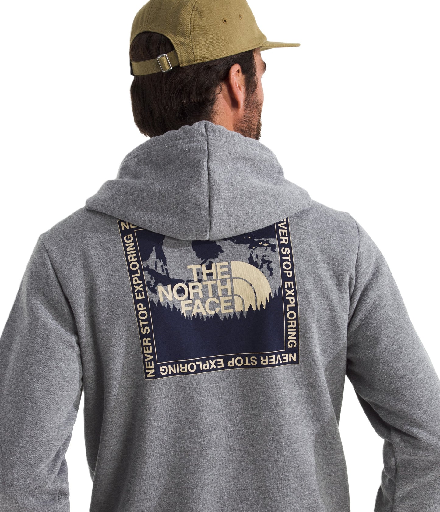 Person wearing a gray hoodie with a square graphic on the back featuring "THE NORTH FACE" above trees with "NEVER STOP EXPLORING" around the square, and a tan baseball cap.