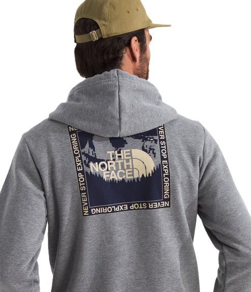 Person wearing a gray hoodie with a square graphic on the back featuring "THE NORTH FACE" above trees with "NEVER STOP EXPLORING" around the square, and a tan baseball cap.