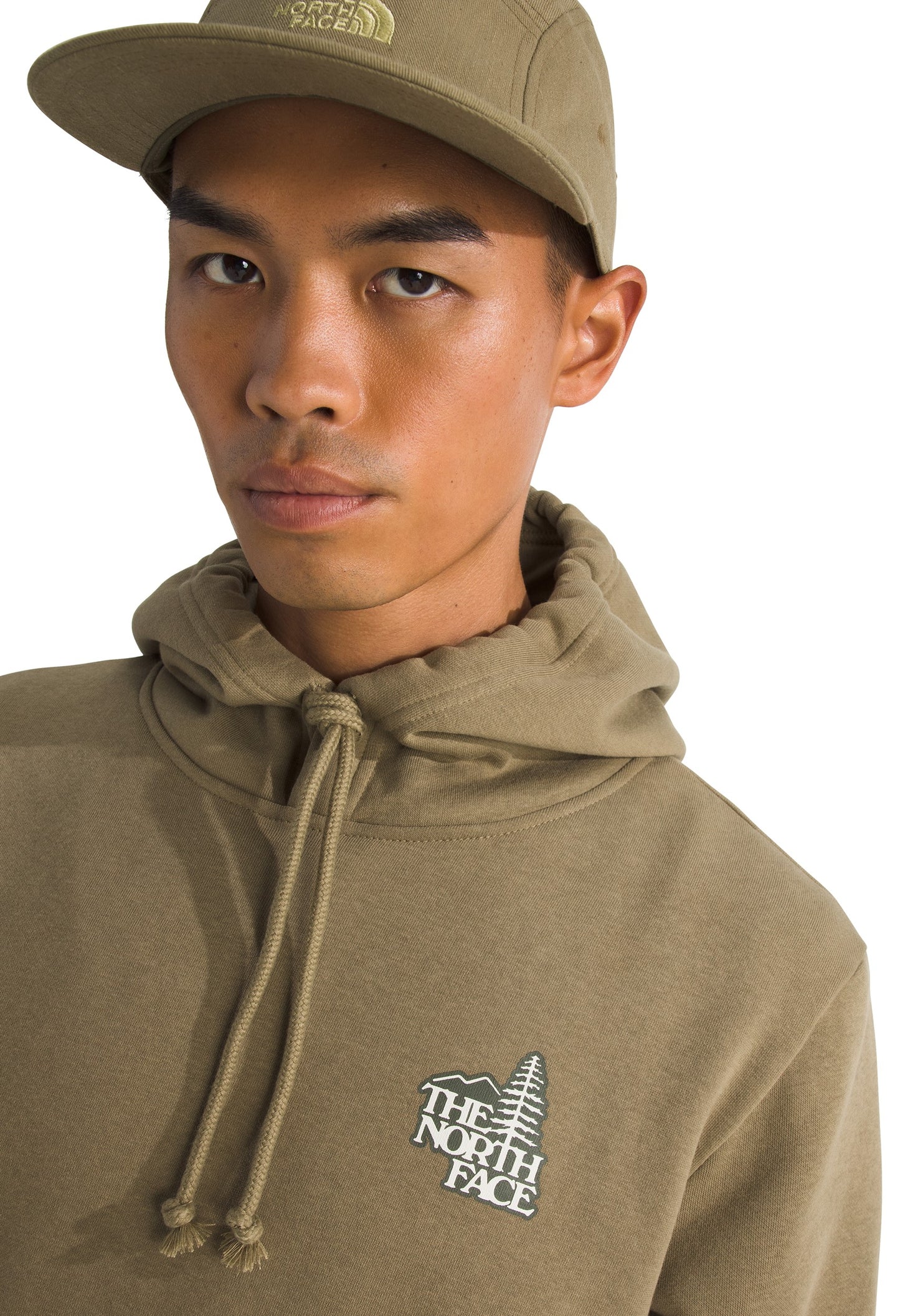 A person wearing a khaki baseball cap and hoodie with drawstrings, featuring a logo of a mountain and tree with the text "THE NORTH FACE".