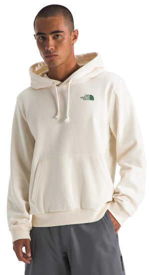 A person wearing a cream-colored hooded sweatshirt with a small green logo on the chest and grey shorts.