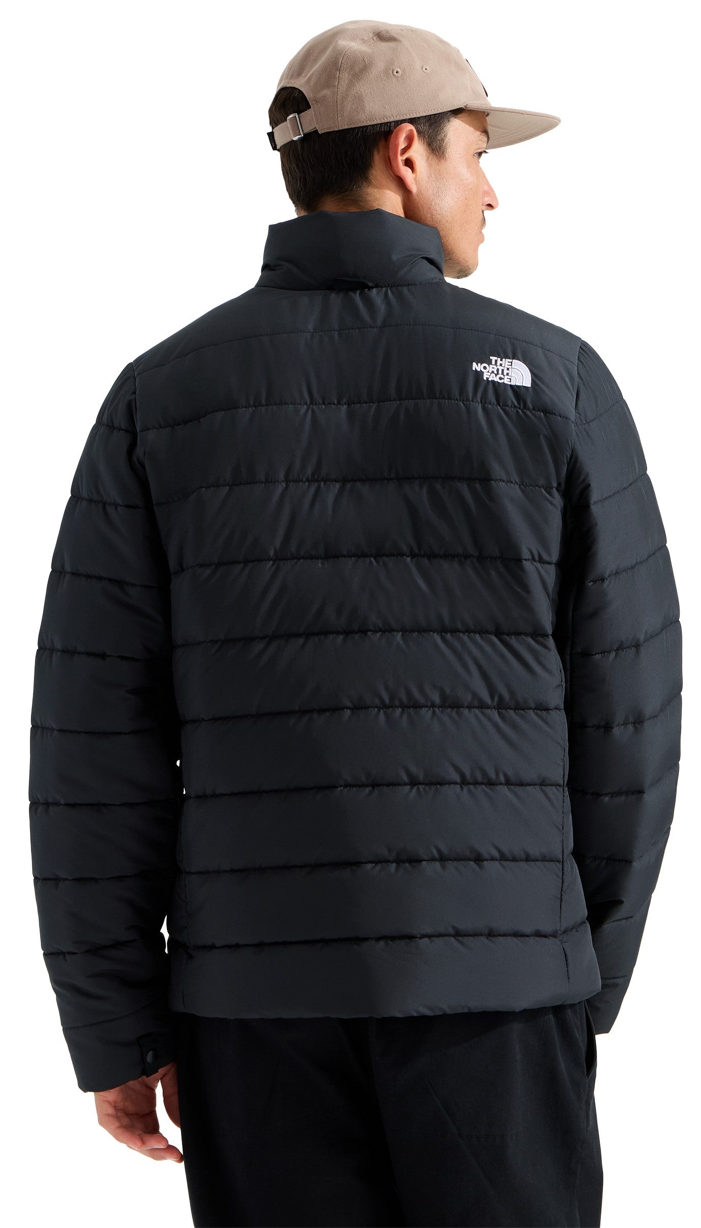 A man wearing a tan cap and a black puffer jacket viewed from behind, featuring horizontal quilting and a white logo on the upper right shoulder.