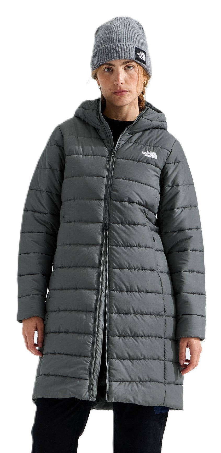 A woman wearing a knee-length, quilted, dark grey hooded puffer jacket and a matching grey ribbed knit beanie, with both items featuring The North Face branding.
